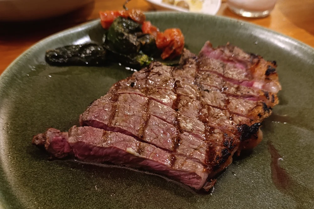 Juicy grilled steak, medium-rare and sliced, served with roasted vegetables on a green plate at Canalha Restaurant in Tavira.