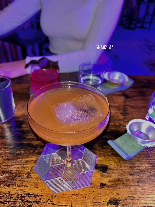 A signature shimmery cocktail served over a large ice cube in a coupe glass at Sneaky Sip cocktail bar in Lisbon.