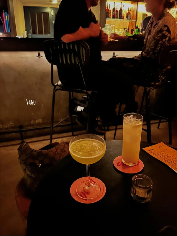 A yellow cocktail in a coupe glass on a table in the cozy, dimly lit atmosphere of Vago cocktail bar in Lisbon.