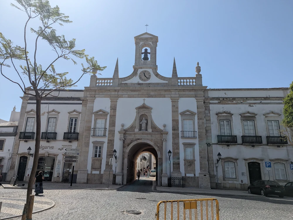 The historic Arco da Vila, the grand neoclassical gateway to Faro's Old Town, seen from the cobblestone street.
