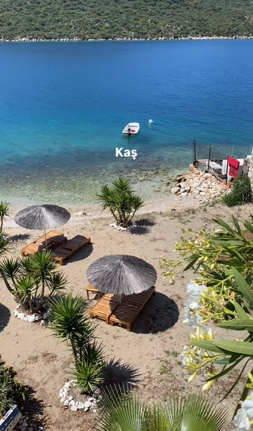 A peaceful beach with straw umbrellas and lounge chairs overlooking the incredibly clear, blue Mediterranean Sea in Kaş, Turkey.
