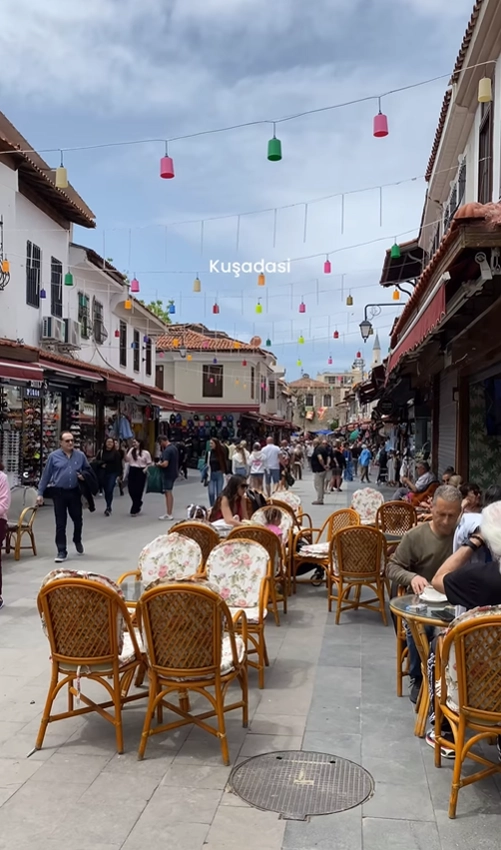 A vibrant street in the old town of Kuşadası, Turkey, filled with people enjoying outdoor cafes under colorful lanterns.