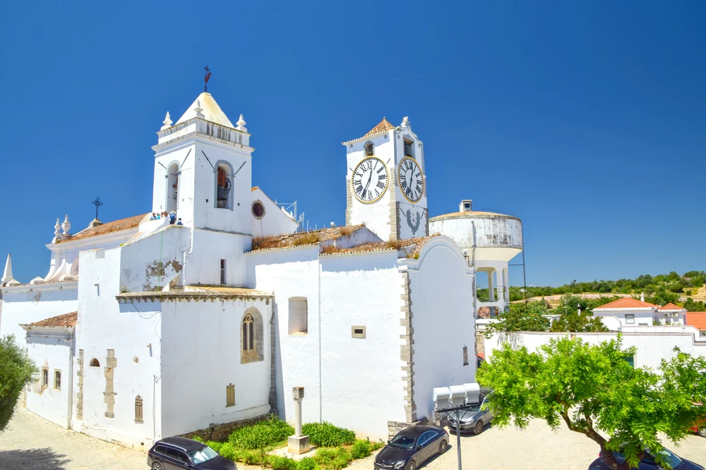 Bright white facade, bell tower, and clock tower of Igreja de Santa Maria do Castelo, a historic church landmark in Tavira.