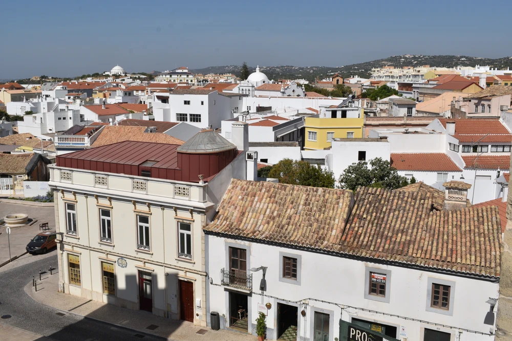 An elevated view over the city of Loulé, Portugal, showing traditional whitewashed buildings with terracotta-tiled roofs under a clear blue sky
