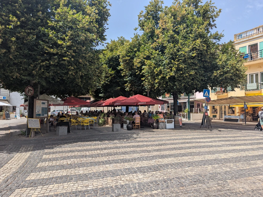 The town square of Largo dos Chorões in Monchique, showing the patterned cobblestone street and a busy outdoor cafe.