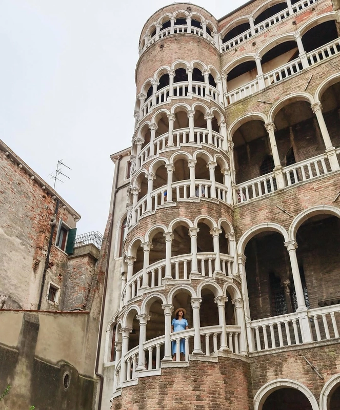 A woman stands on the balcony of the unique spiral staircase, the Scala Contarini del Bovolo, at the Palazzo Contarini in Venice.