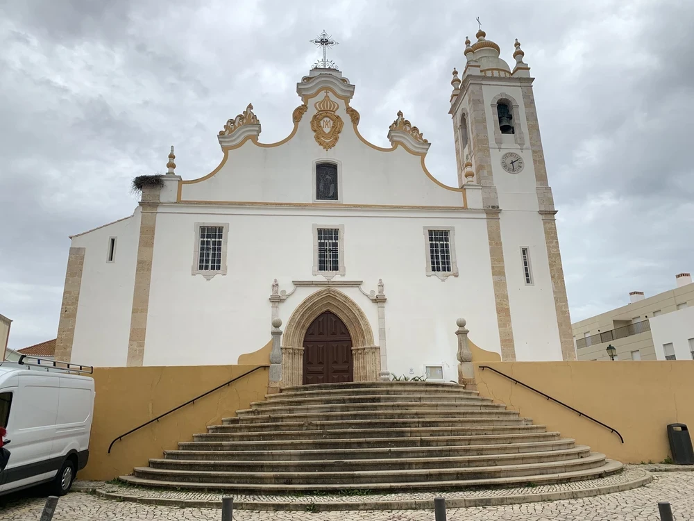 Front view of Igreja de Nossa Senhora da Conceição in Portimão with wide stone steps and baroque details under cloudy sky