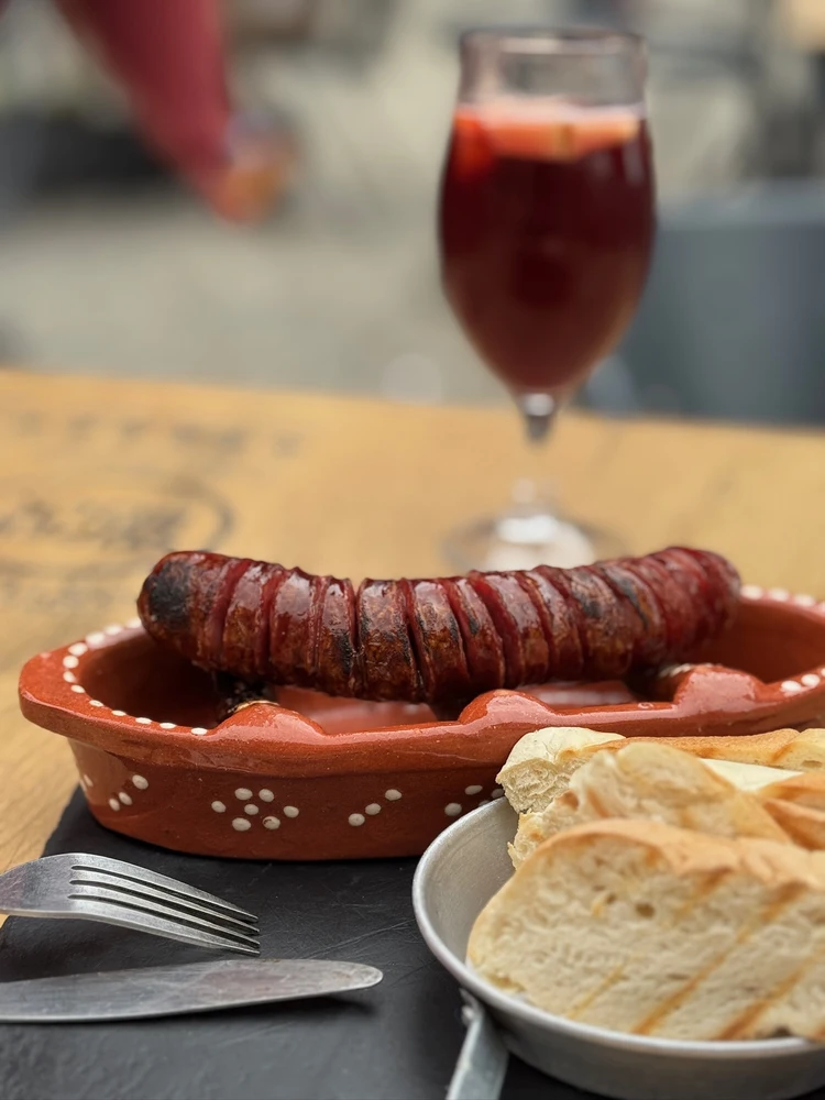 Traditional flame-grilled chouriço sausage served in a clay dish with bread, a popular tasting on a food tour in Porto.
