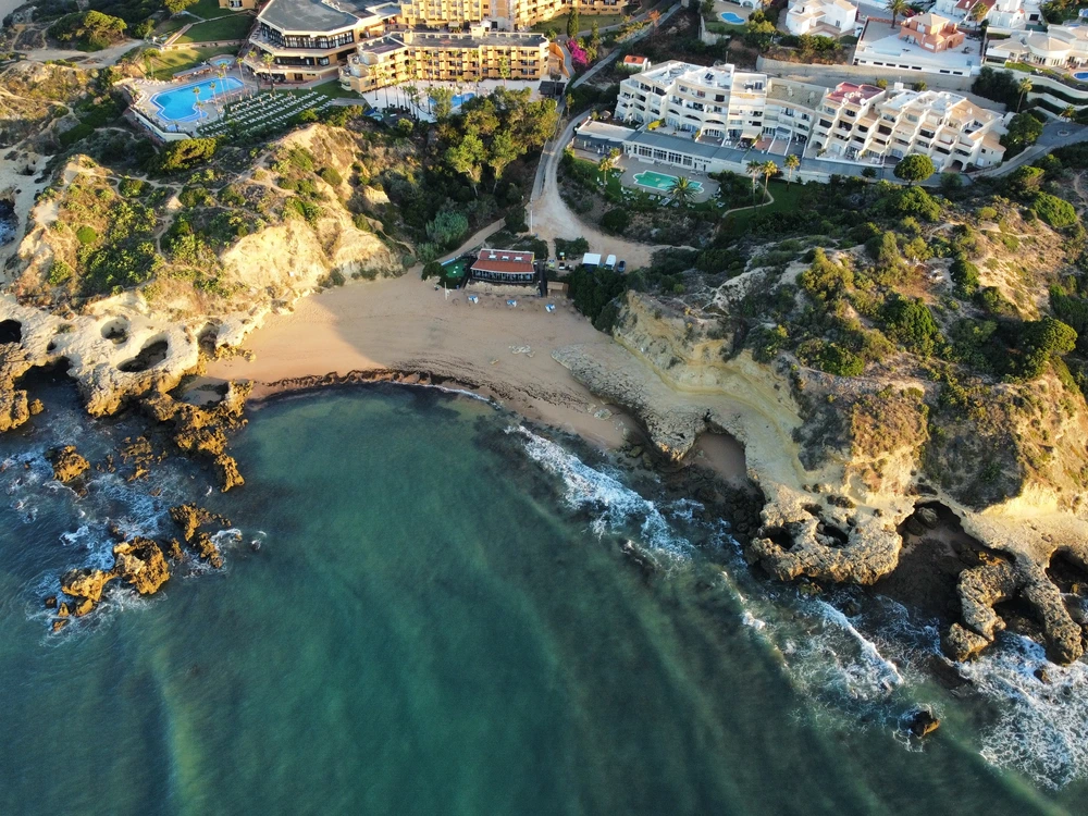 Aerial view of the secluded Praia dos Aveiros beach in Albufeira, a beautiful cove with golden sand and turquoise water surrounded by cliffs.