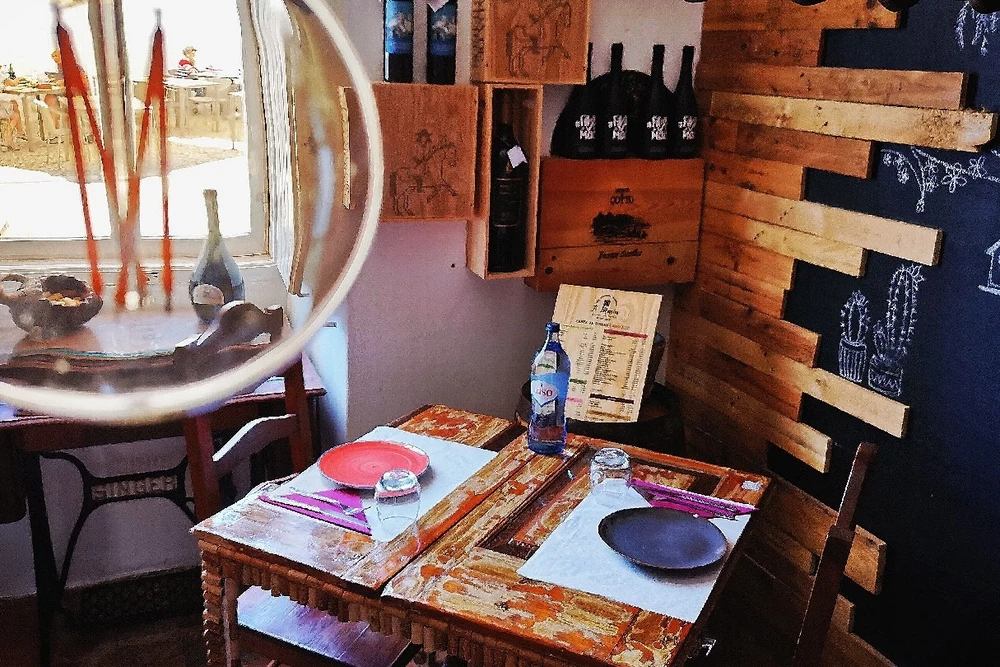 Rustic and artistic interior design of Tavira Maria Tapas e Garrafeira restaurant, with wooden planks and wine bottles on display.