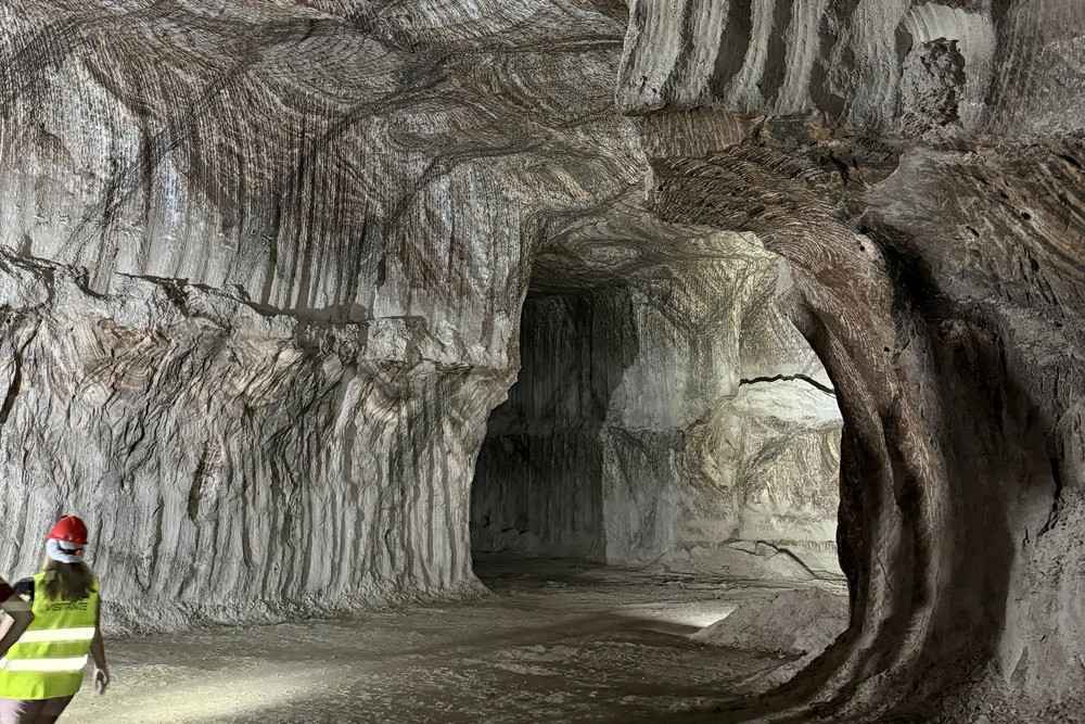 The interior of the deep Rock Salt Mine Tour near Loulé, Portugal, showcasing the dramatic, striated walls of the ancient salt deposit and a guide in a high-visibility vest.