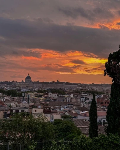 A dramatic orange sunset over the skyline of Rome, with the dome of St. Peter's Basilica visible in the distance, showcasing one of the best non-touristy things to do in the city.
