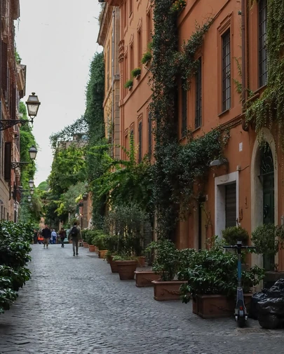A picturesque, narrow cobblestone street in Rome, lined with orange buildings and lush greenery, captures the essence of doing non-touristy things like exploring the city's authentic character.
