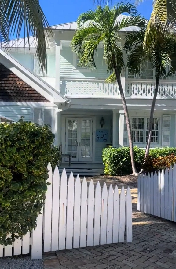Exterior of a luxury two-story guest cottage at Sunset Key, Key West, with a white picket fence and tropical palm trees.