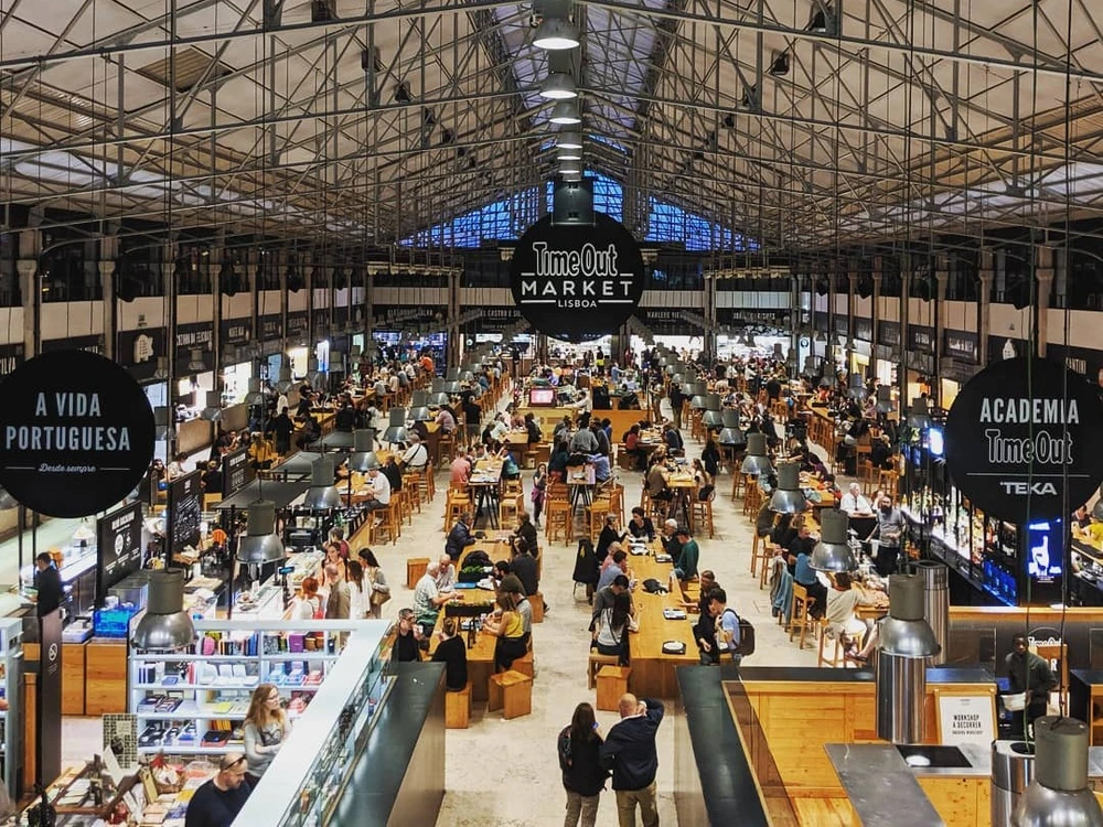 An overhead view of the bustling and vibrant Time Out Market in Lisbon, showing the vast food hall filled with various food stalls and people dining.