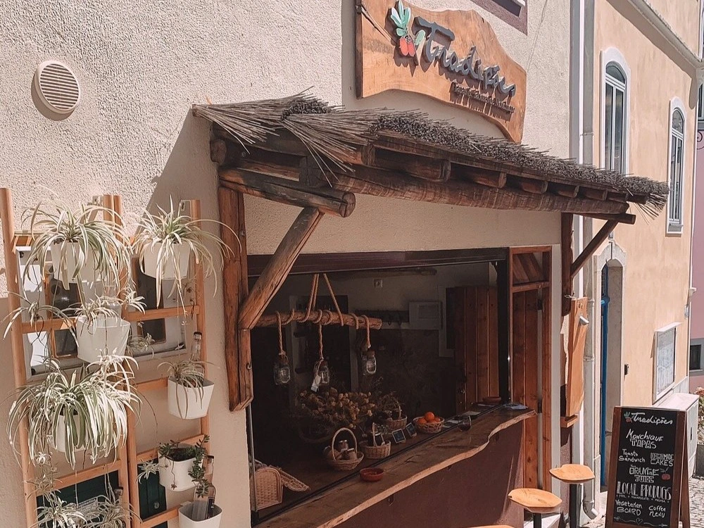 The charming storefront of Tradições restaurant in Monchique, featuring a rustic thatched awning over a service window and potted plants.
