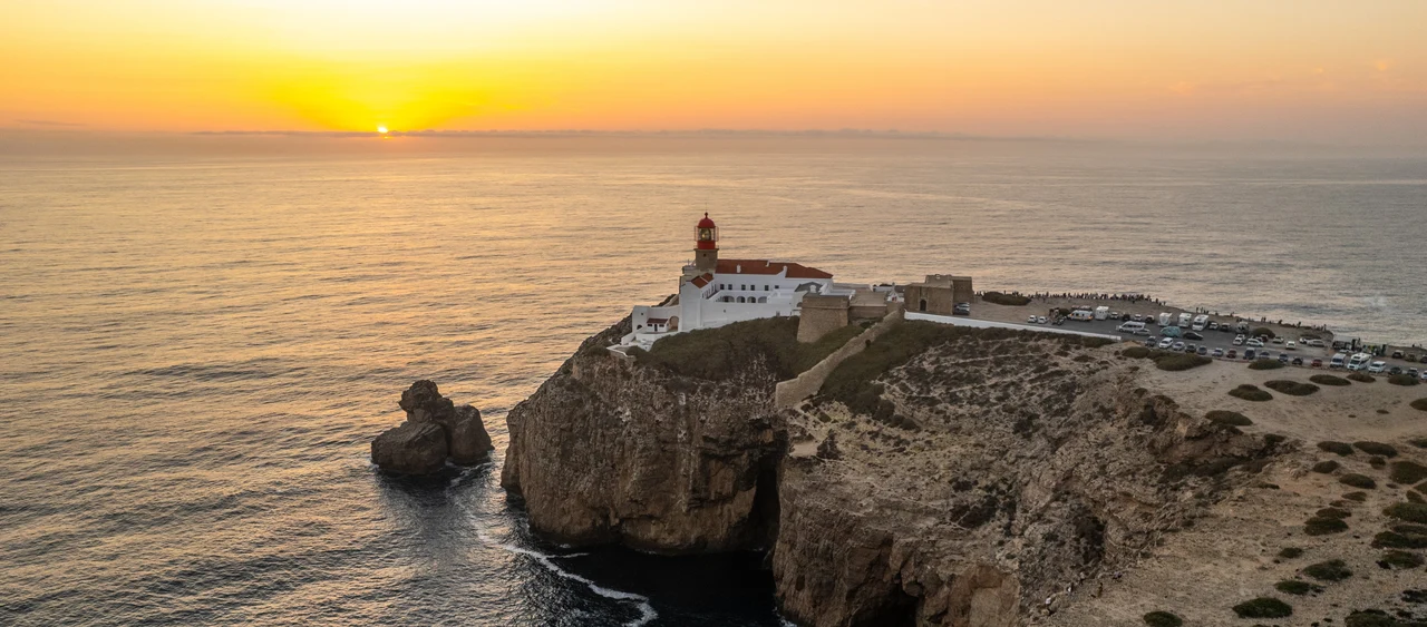 The stunning Cape St. Vincent lighthouse in Sagres, perched on a cliffside as the sun sets over the Atlantic Ocean.
