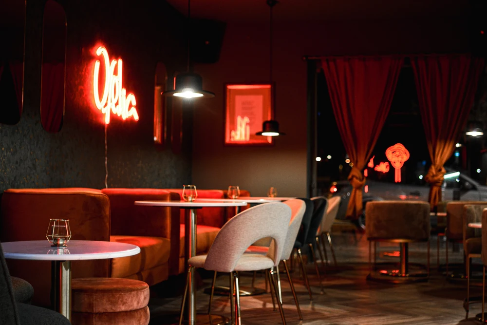 Stylish interior of Afelia Art Cocktail Bar in Tavira, with red velvet seating, modern lighting, and a bright red neon sign.