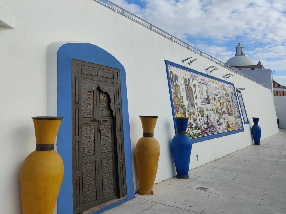 The unique exterior of the Albufeira Archeological Museum, featuring a traditional carved wooden door, large decorative vases, and historic Portuguese tiles.