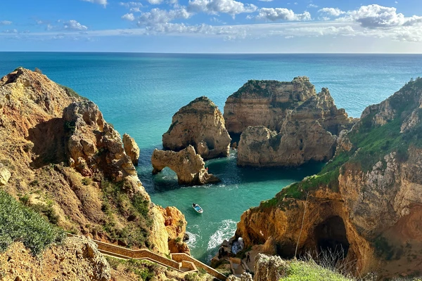 Dramatic limestone cliffs and turquoise waters at Ponta da Piedade in Lagos, Algarve, Portugal, with a boat navigating through rock formations.