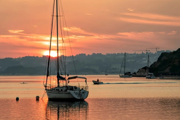 Sailboats and fishing boats on calm waters at sunset in Alvor, Algarve, Portugal, with golden reflections on the horizon.
