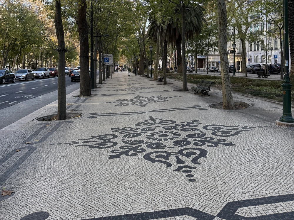 The iconic Portuguese cobblestone pavement with a beautiful black floral pattern on the tree-lined sidewalk of Avenida da Liberdade in Lisbon.