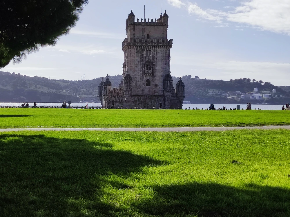 The historic Belém Tower, a famous landmark in Lisbon, viewed from the lush green lawn of the adjacent garden on a sunny day.