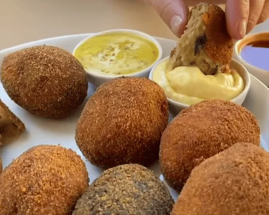 Close-up of a plate piled high with various Portuguese croquetes being dipped into sauce, showcasing the best croquetes in Lisbon.