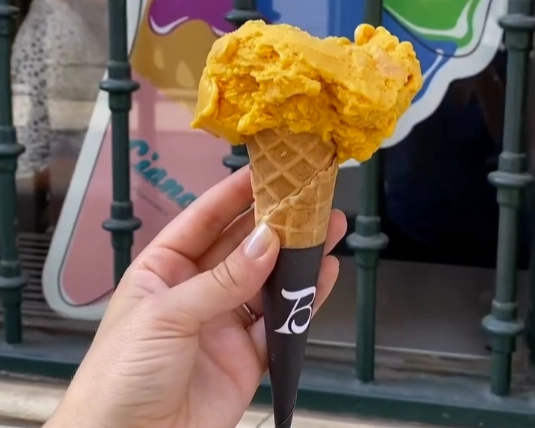 A hand holding a bright orange mango ice cream cone from Bizzarro Gelato in Cais do Sodré, Lisbon.