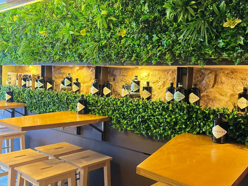 The stylish interior of the Botanical Den cocktail bar in Lisbon, featuring a stunning wall of lush greenery and an artful display of Hendrick's Gin bottles.