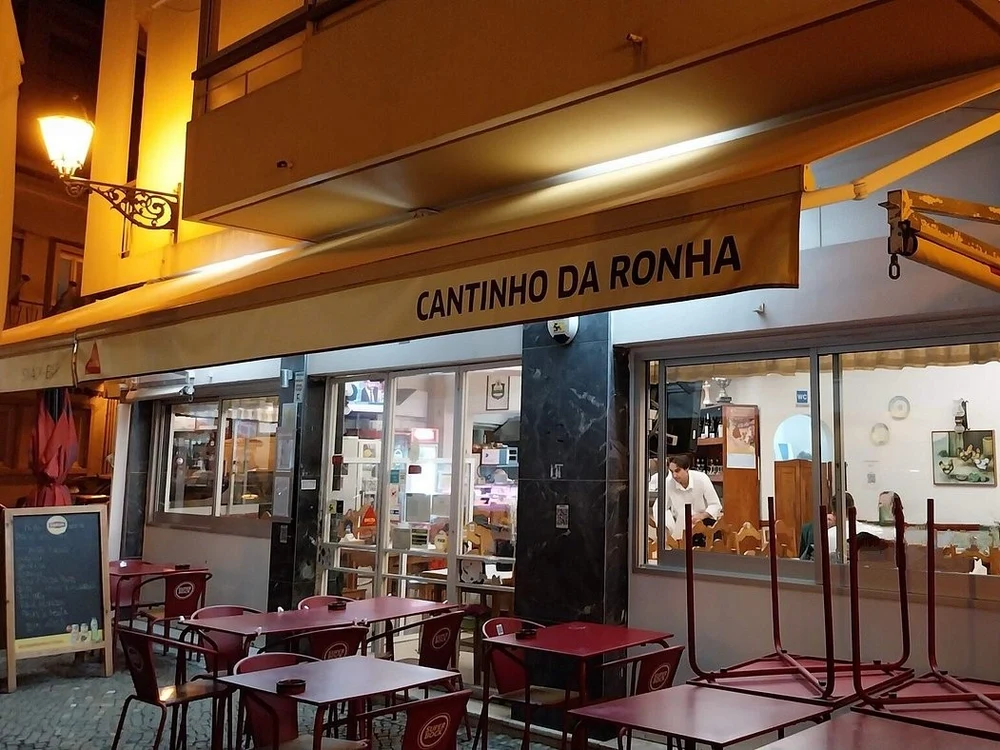 The warmly lit exterior of Cantinho da Ronha, a traditional Portuguese restaurant in Faro, with its outdoor patio at night.