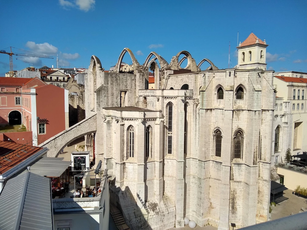 The iconic, roofless Gothic arches of the historic Carmo Convent in Lisbon, standing starkly against a clear blue sky.