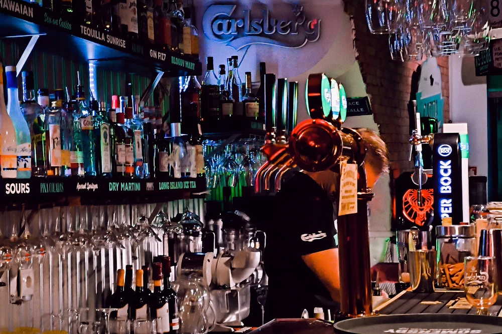 Close-up of a brightly lit bar area with beer taps, liquor bottles, and a barman working at Catita & Companhia in Olhao, Portugal.