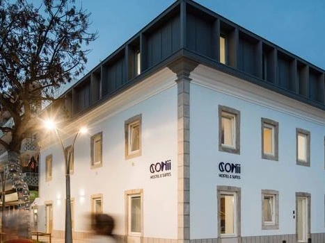 The modern, white exterior of the Conii Hostel & Suites building on a street corner in Quarteira.