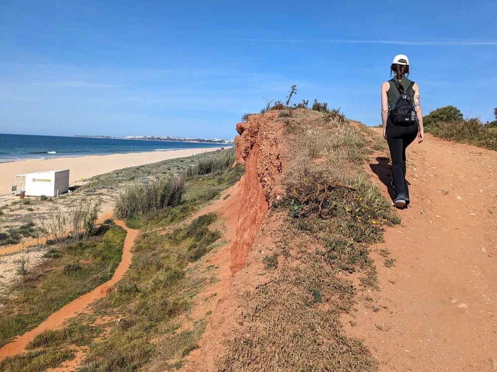 A hiker walking along the scenic clifftop trail of Estrada da Rocha Baixinha, with stunning views of the coastline in Vilamoura.
