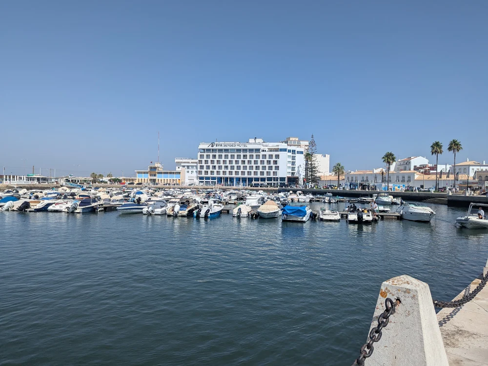 View of the bustling Faro Marina, with boats moored in the harbor and the Hotel Eva Senses in the background.