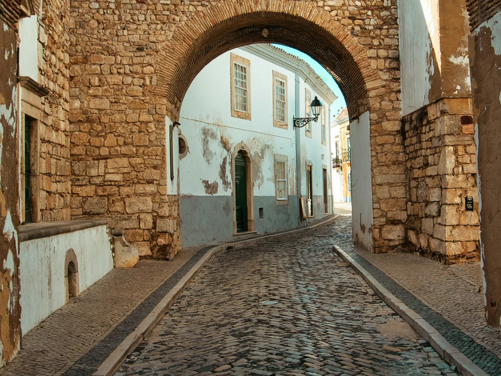 A charming cobblestone street viewed through the historic stone Arco do Repouso in Faro's Old Town (Cidade Velha).