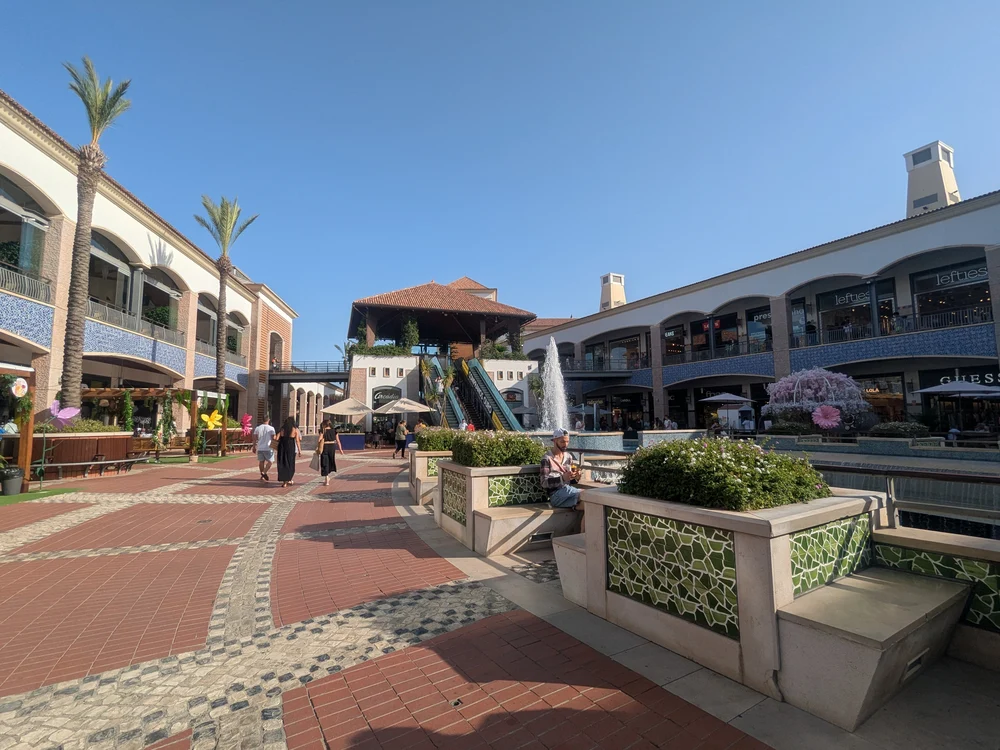 Shoppers enjoying a sunny day at the open-air Forum Algarve shopping mall in Faro, with its fountains and palm trees.