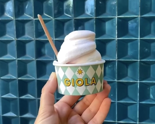 A cup of light pink artisanal gelato with a wooden spoon from GIOLA GELATO in the Alfama district of Lisbon.