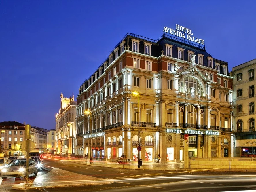 A stunning night-time view of the grand and beautifully illuminated historic facade of the luxurious Hotel Avenida Palace in the heart of Lisbon.
