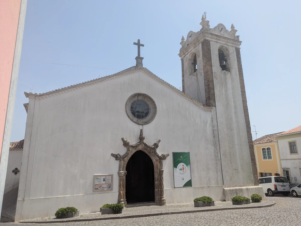 The white facade of the historic Igreja Paroquial de Monchique, showing its ornate Manueline doorway and stone bell tower.
