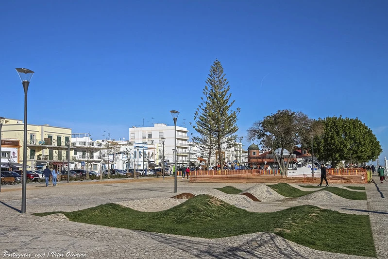 olhao.webp Wide shot of the Jardim do Pescador (Fisherman's Garden) public square with modern grassy mounds and palm trees in Olhao, Portugal.