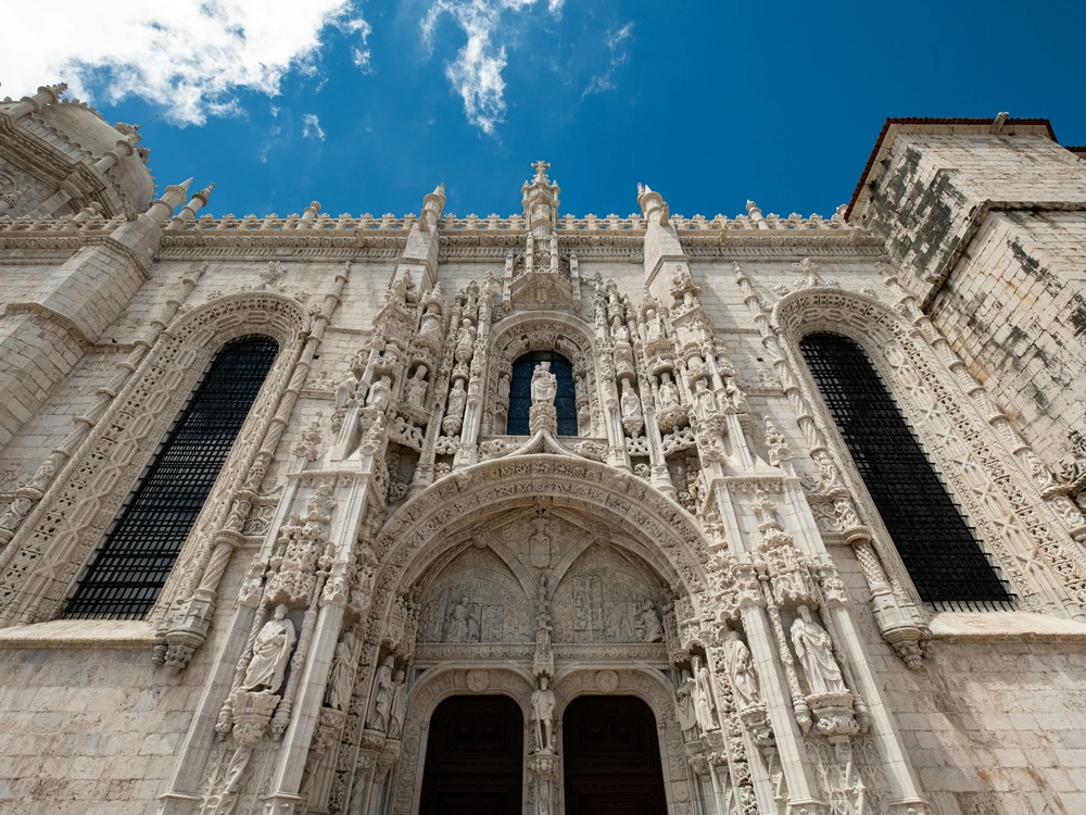 A low-angle shot showcasing the incredibly detailed and ornate Manueline-style stone carvings on the grand entrance of the Jerónimos Monastery in Lisbon.