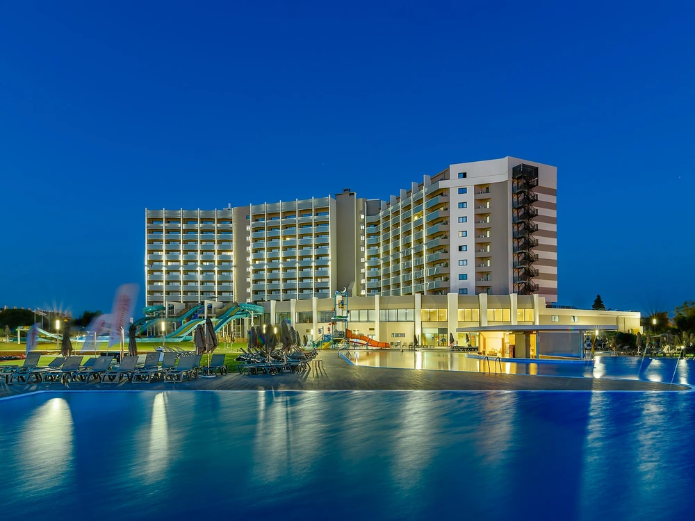 The impressive Jupiter Albufeira Hotel lit up at night, with its large swimming pool reflecting the bright lights of the family-friendly resort.