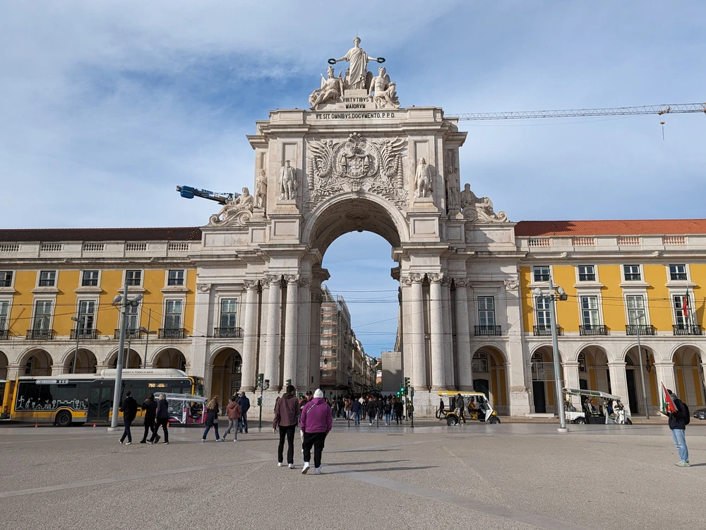The magnificent Arco da Rua Augusta triumphal arch in Lisbon's Praça do Comércio, with tourists and locals walking through the square.