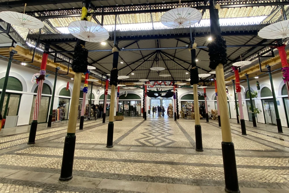 The spacious, ornate interior of the historic Mercado da Ribeira in Tavira, decorated with white umbrellas and columns.