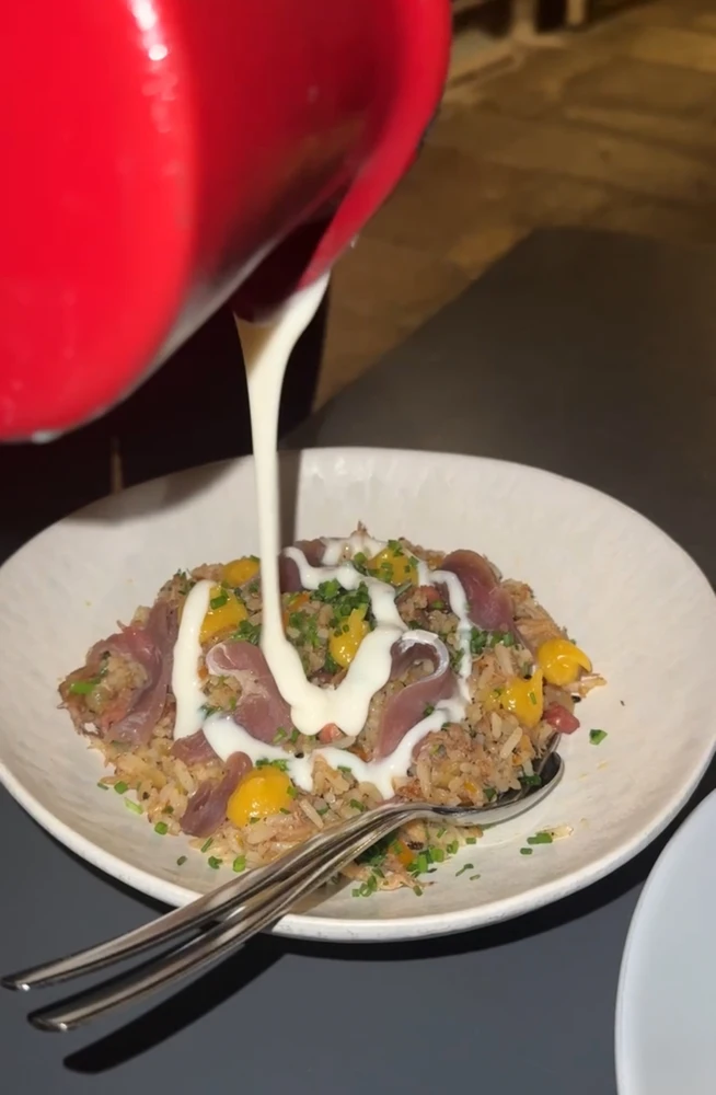 A specialty rice dish being finished with a creamy sauce at Muro do Bacalhau, a riverside restaurant in Porto.