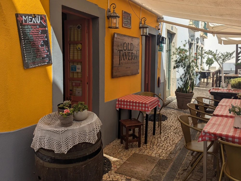 The rustic, inviting entrance to Old Tavern restaurant in Faro, with its charming checkered tablecloths and barrel table.