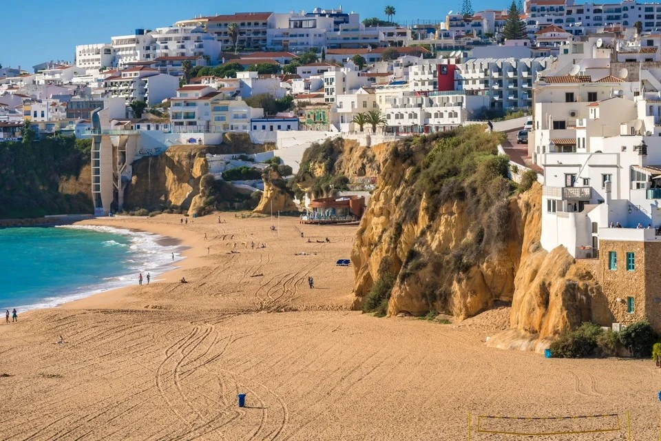 Scenic view of Pescadores Beach in Albufeira (popular day trip from Olhao) featuring golden cliffs, sand, and white buildings lining the hillside.
