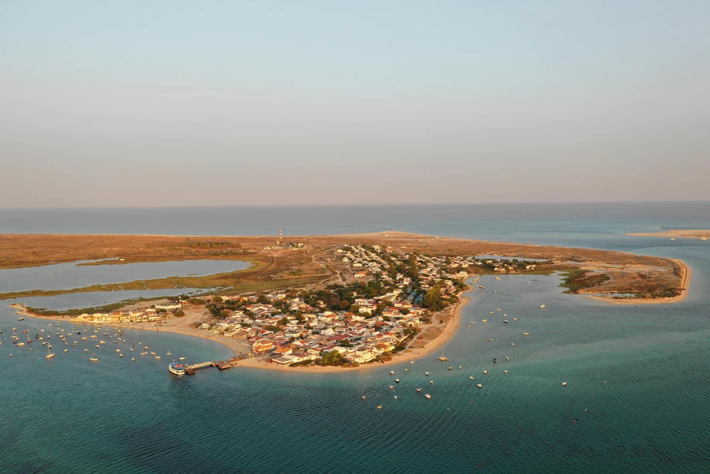 Aerial view of Armona Island with traditional white houses and boats in the calm turquoise waters of Olhao, Portugal, at sunset.